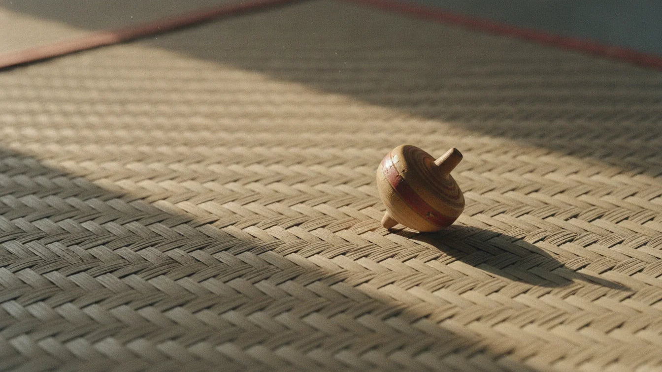 A small hand-turned wooden spinning top with one red lacquer band lying on a woven mat in morning light
